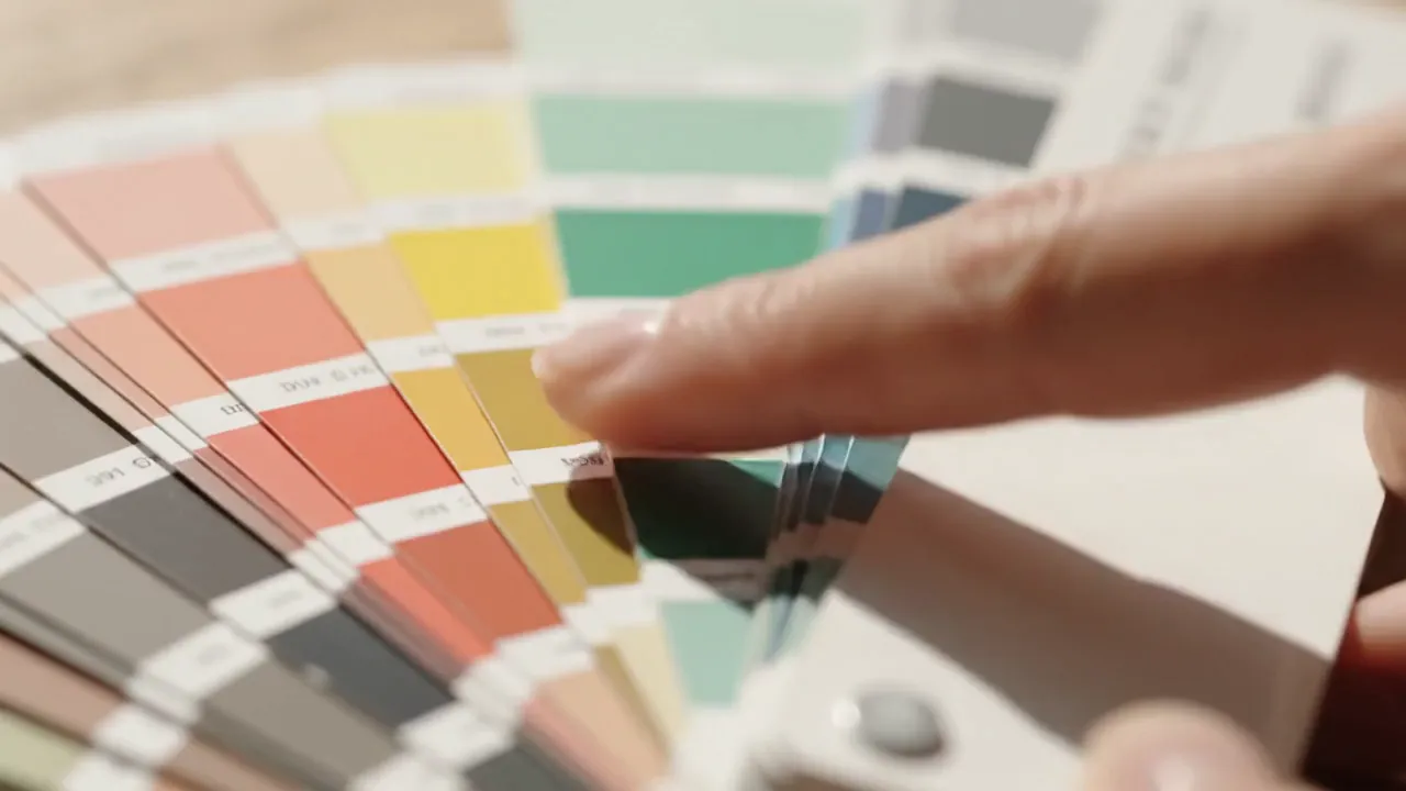 A hand selecting a colour from a fanned swatch book