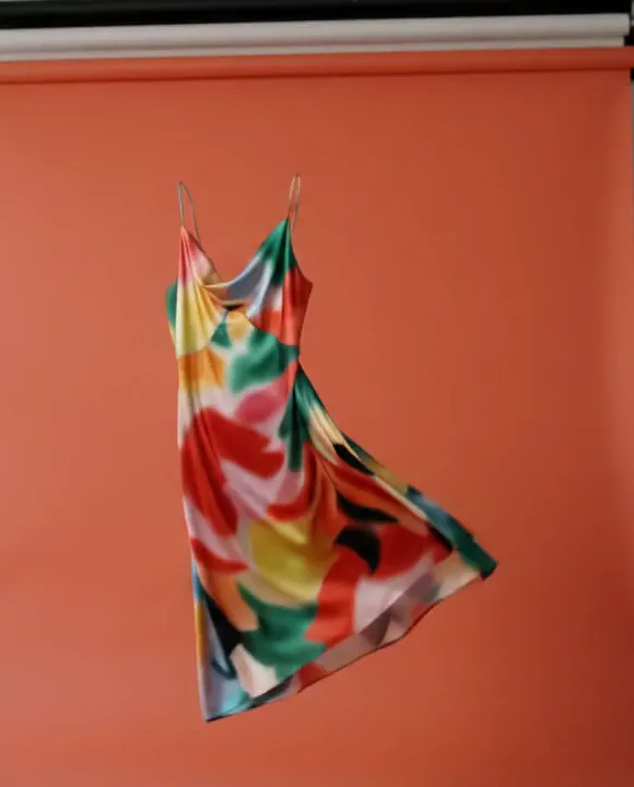 A printed silk dress suspended against a coral studio backdrop